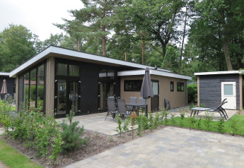 Modern lodge at Holiday Park De Rimboe & De Woeste Hoogte 25 featuring a patio, outdoor seating, and lush greenery.