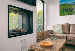 Gemütliches Wohnzimmer im Holiday Park Zeedijk 1, Niederlande, mit Kamin, Sofa und Holztisch.