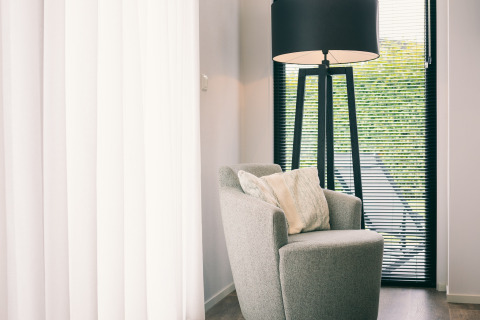 Sillón y lámpara de pie junto a una ventana con persianas en Holiday Park «Zeedijk 1» en Países Bajos.