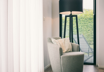 Modern armchair and floor lamp by a window with blinds at Holiday Park «Zeedijk 1» in the Netherlands.