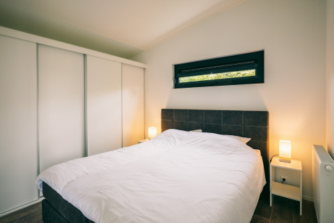 Modern bedroom with a double bed, bedside tables, and wardrobe at Holiday Park «Zeedijk 1» in the Netherlands.