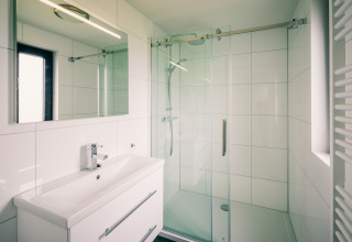 Moderne badeværelse med glasbruser, spejl og hvidt vaskeskab i Holiday Park Zeedijk 1, Holland.