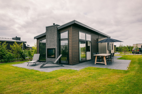 Moderne træhytte med terrasse og udendørs spisearrangement i Holiday Park Zeedijk 1, Holland, omgivet af grønne områder.