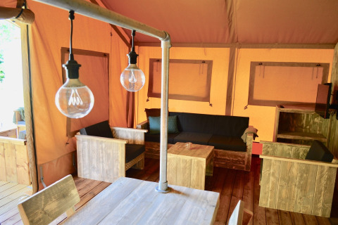 Interior of a safari tent featuring rustic wooden furniture, a cozy seating area, and hanging light bulbs.