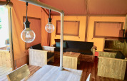 Interno di una tenda safari con arredi rustici in legno, area salotto e lampadine a sospensione.