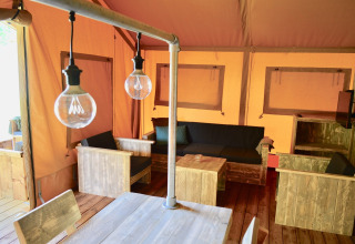 Interior of a safari tent featuring rustic wooden furniture, a cozy seating area, and hanging light bulbs.