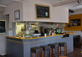 Foto di un accogliente bar con sgabelli, bicchieri appesi e lavagna del menu in una tenda safari.