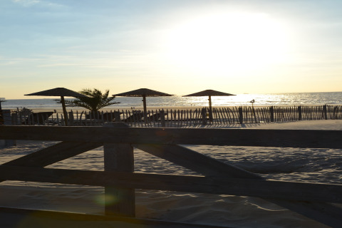 Sunset view from a safari tent at the beach, showing parasols, sandy dunes, and a wooden fence in front.