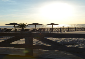 Tramonto visto da una tenda safari sulla spiaggia con ombrelloni, dune di sabbia e una recinzione di legno.
