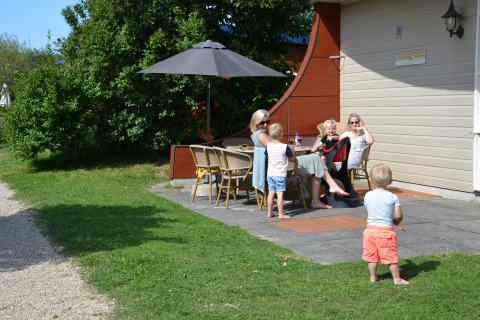 Family relaxing outside under parasol at Beach Park Vlugtenburg 13 safari tent in the Netherlands.