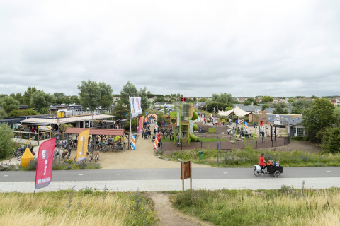 Photo of a playground and café at a safari tent site with bikes and families on a cloudy day.