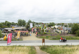 Photo of a playground and café at a safari tent site with bikes and families on a cloudy day.