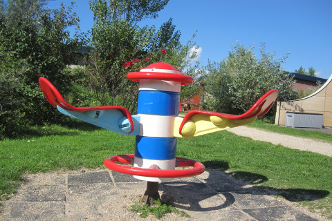 Outdoor playground equipment with colorful seats and handles, photographed near a safari tent location.
