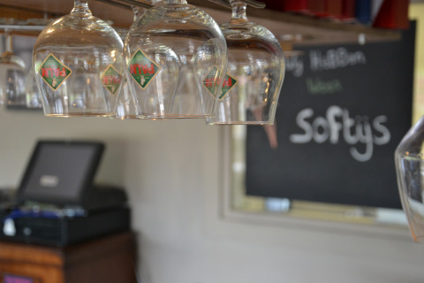A row of upside-down beer glasses in a safari tent bar, with a blackboard and cash register behind.