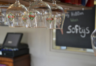 A row of upside-down beer glasses in a safari tent bar, with a blackboard and cash register behind.