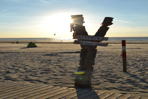 Sunset on the beach with a sign reading 'ELEMENTS' and 'give good vibes' near a safari tent.