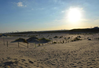 Photo taken at a safari tent site on a sandy beach with dunes, fencing, and the sun setting behind.