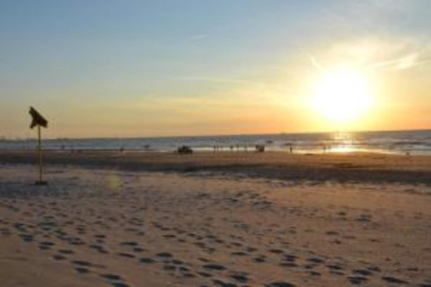Atardecer en una tranquila playa arenosa, huellas en la arena y señal de tienda safari a la izquierda.
