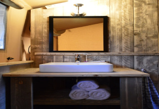 Wood-paneled bathroom in a safari tent at Beach Park Vlugtenburg 13, Netherlands, with sink and towels.