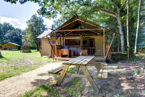 Safari tent Country Estate Gerner 8 set in wooded surroundings with wooden benches and green lawns.