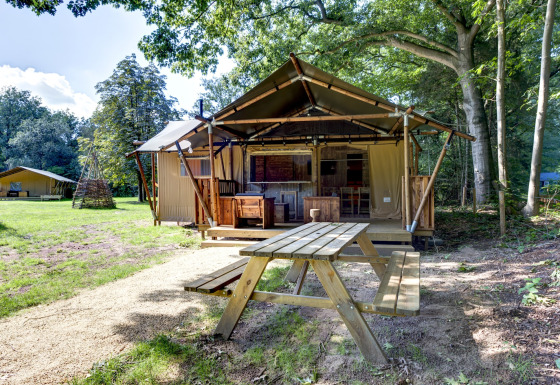 Safari tent Country Estate Gerner 8 set in wooded surroundings with wooden benches and green lawns.