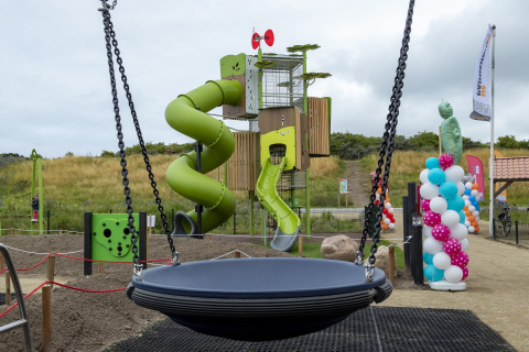 Playground with green spiral slide and large round swing at Beach Park Vlugtenburg 12, Netherlands, cloudy sky.