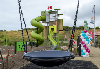 Parco giochi con scivolo verde e grande altalena a Beach Park Vlugtenburg 12, Paesi Bassi, cielo nuvoloso.
