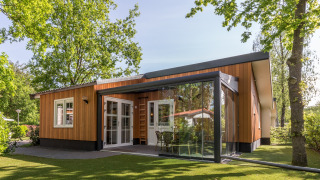 Lodge moderno en Residence De Eese 3 con fachada de madera y paredes de cristal, rodeado de vegetación.