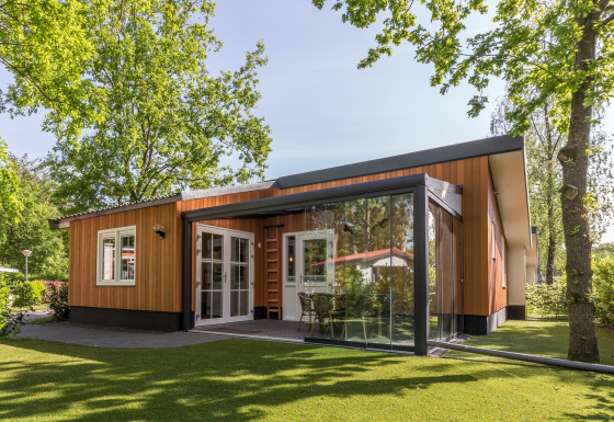 Moderne lodge bij Residence De Eese 3 met houten gevel, glazen wanden en groene, bosrijke omgeving.