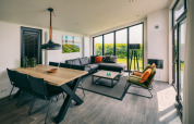 Modern living room at Holiday Park «Zeedijk 3» in Netherlands with large windows, dining table and sofa.