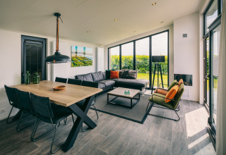 Modernes Wohnzimmer im Holiday Park «Zeedijk 3» Niederlande mit großen Fenstern, Esstisch und Sofa.