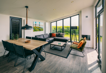 Modern living room at Holiday Park «Zeedijk 3» in Netherlands with large windows, dining table and sofa.