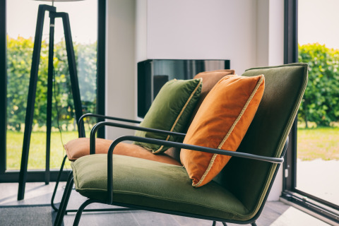 Modern lounge chairs with green and orange cushions by large windows at Holiday Park Zeedijk 3, Netherlands.