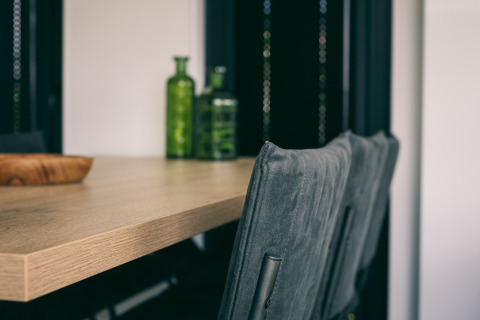 Primer plano de mesa de madera con botellas verdes y sillas grises en Holiday Park Zeedijk 3, Países Bajos.