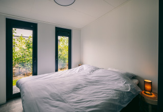 Modern bedroom at Holiday Park Zeedijk 3 in the Netherlands with large windows and cozy bedside lighting.