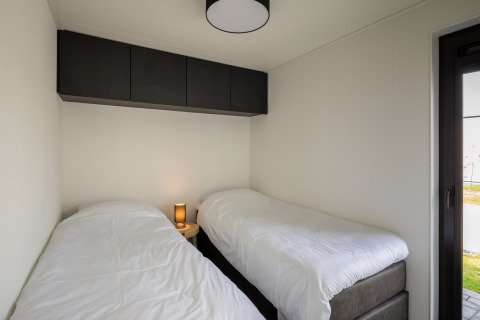 Dormitorio moderno con dos camas individuales, armarios oscuros y lámpara en Holiday Park Zeedijk 3, Países Bajos.