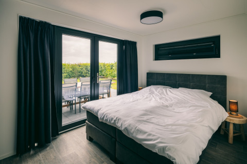 Camera da letto al Holiday Park «Zeedijk 3» nei Paesi Bassi, con letto matrimoniale e terrazza sul verde.