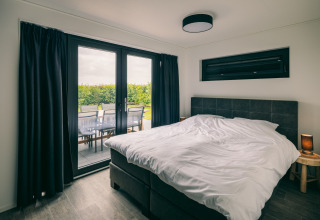Camera da letto al Holiday Park «Zeedijk 3» nei Paesi Bassi, con letto matrimoniale e terrazza sul verde.