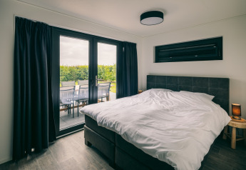 Bedroom at Holiday Park «Zeedijk 3» in the Netherlands, with double bed and patio overlooking greenery.