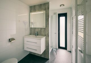 Baño moderno en Holiday Park Zeedijk 3, Países Bajos, con ducha, lavabo, espejo y ventana alta.