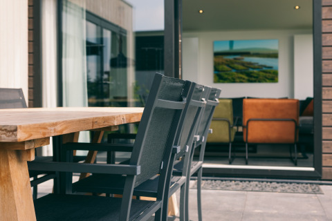 Outdoor dining table and chairs on patio at Holiday Park «Zeedijk 3» with view into the living room.