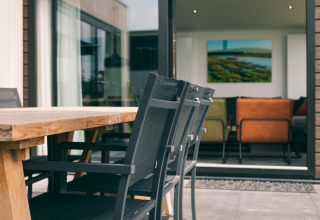Mesa y sillas exteriores en la terraza de Holiday Park «Zeedijk 3», con vista al salón interior moderno.
