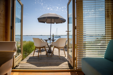 Vue depuis une tiny house à Eco Resort Grevelingenstrand, Pays-Bas, avec terrasse, parasol et lac.