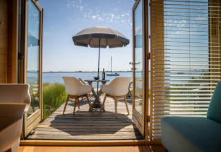 Vue depuis une tiny house à Eco Resort Grevelingenstrand, Pays-Bas, avec terrasse, parasol et lac.