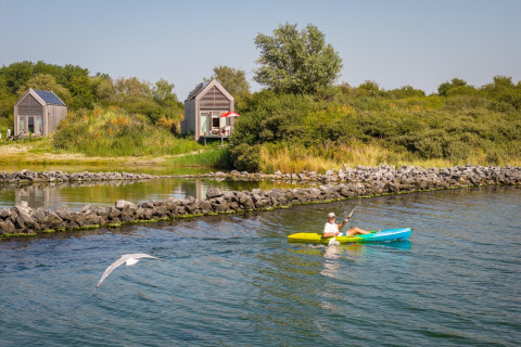 Personne en kayak devant des tiny houses à l’Eco Resort Grevelingenstrand aux Pays-Bas, entouré de nature.