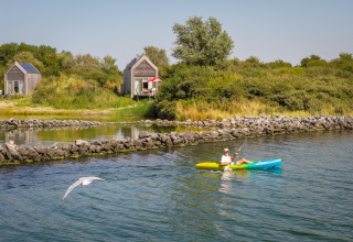 Personne en kayak devant des tiny houses à l’Eco Resort Grevelingenstrand aux Pays-Bas, entouré de nature.