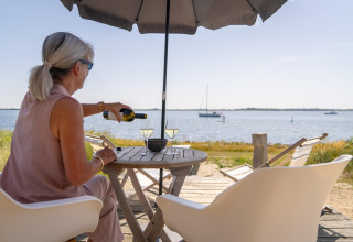 Femme verse du vin sous un parasol à l’Eco Resort Grevelingenstrand, aux Pays-Bas, face à la mer.