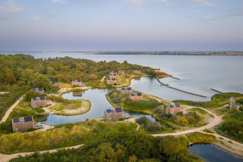 Vue aérienne de tiny houses au bord d’un lac à l’Eco Resort Grevelingenstrand, entourées de nature aux Pays-Bas.
