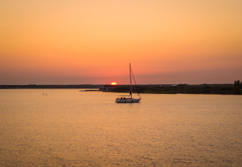Smuk solnedgang over vandet ved Eco Resort Grevelingenstrand i Holland med en sejlbåd i forgrunden.