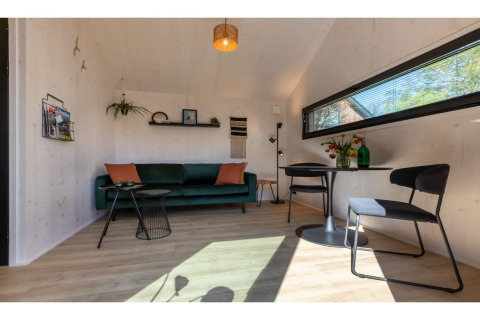 Gezellige leefruimte in Tinyhouse «La Mouette» in Nederland met groene zetel, eettafel en raam.
